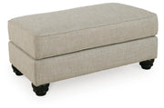 Ashley Furniture Asanti Ottoman with plush fabric and wooden legs, shown from an angled side view.