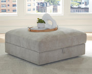 Ashley Furniture Aslan Court Ottoman with storage, upholstered fabric, and wooden legs, shown closed in a modern living room setting.