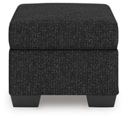 Ashley Furniture Jasmine Peaks Ottoman with fabric upholstery and wooden legs, shown from a side angle.