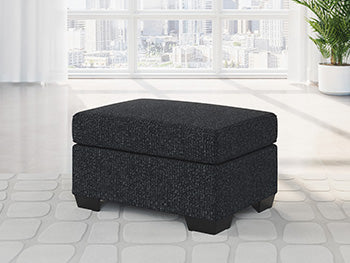 Ashley Furniture Jasmine Peaks Ottoman showing plush fabric and wooden legs in a cozy living room setting.