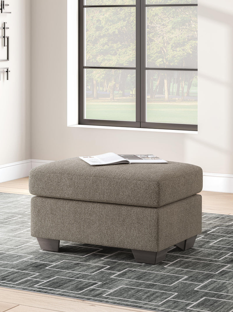 Ashley Furniture Triston-Peaks Ottoman in neutral fabric with wooden block legs, showcasing a versatile and stylish accent piece.