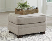Ashley Furniture Gaelon Ottoman with soft fabric upholstery and wooden block feet, serving as a stylish footrest or accent piece.