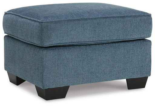Ashley Furniture Cashton Ottoman with upholstered fabric and wooden legs, shown from an angled side view.