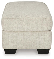 Ashley Furniture Heartcort Ottoman in beige fabric with tufted top and wooden legs, shown from side view.