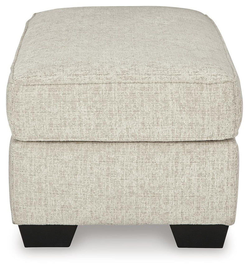 Ashley Furniture Heartcort Ottoman in beige fabric with tufted top and wooden legs, shown from side view.