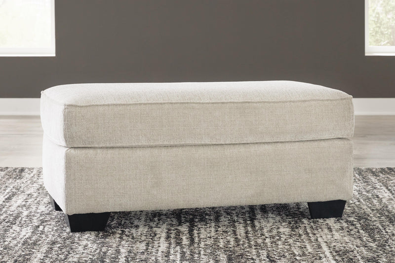 Ashley Furniture Heartcort Ottoman with soft cushioned top and wooden legs, ideal for living room decor.