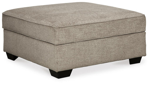 Ashley Furniture Bovarian Ottoman with plush fabric and wooden legs, shown from an angle in a cozy living room setting.