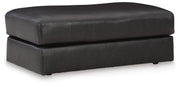 Ashley Furniture Amiata Ottoman showing a plush, upholstered round ottoman with a soft fabric surface and wooden base.