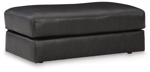 Ashley Furniture Amiata Ottoman showing a plush, upholstered round ottoman with a soft fabric surface and wooden base.