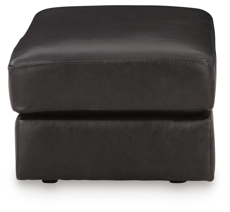 Ashley Furniture Amiata Ottoman, beige fabric with tufted top and wooden legs, shown from a side angle.
