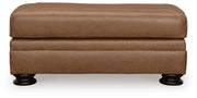 Ashley Furniture Carianna Ottoman with beige fabric and tufted top, shown from a front head-on view.