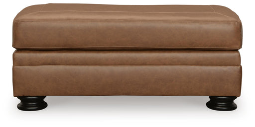 Ashley Furniture Carianna Ottoman with beige fabric and tufted top, shown from a front head-on view.
