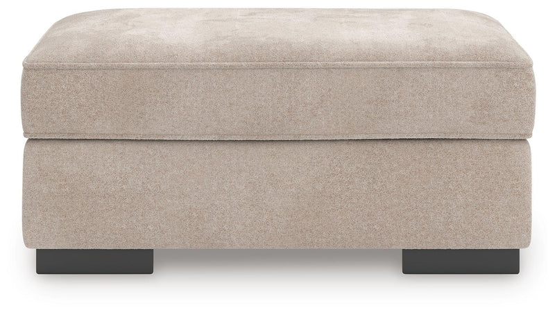 Ashley Furniture high profile ottoman with cushioned top and dark wooden legs, shown in a sleek, modern living room setting.