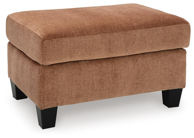 Ashley Furniture Amity Bay Ottoman with fabric upholstery, shown from an angled view, featuring a cushioned top and wooden legs.