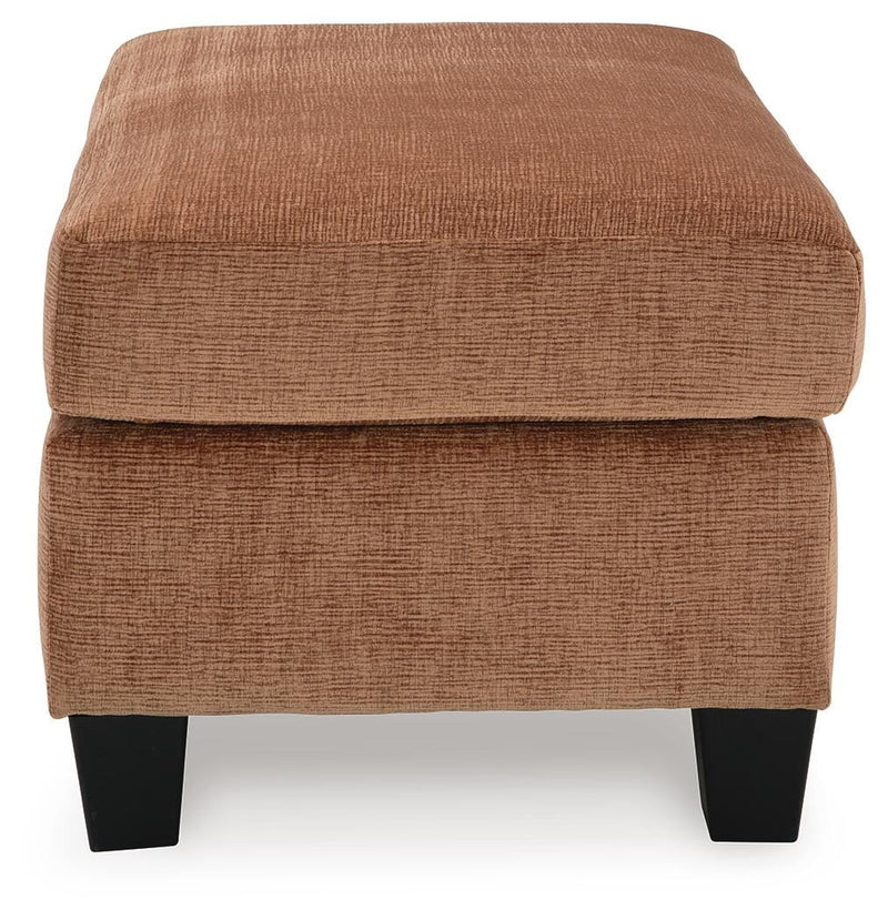 Ashley Furniture Amity Bay Ottoman with plush fabric and storage space, shown from a side angle in a cozy living room setting.