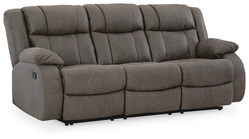 Ashley Furniture First Base reclining sofa in a neutral fabric, shown from a side angle with closed recliner and plush cushions.