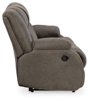 Ashley Furniture First Base reclining sofa with plush cushions and reclining features, shown from the side in a modern living room setting.