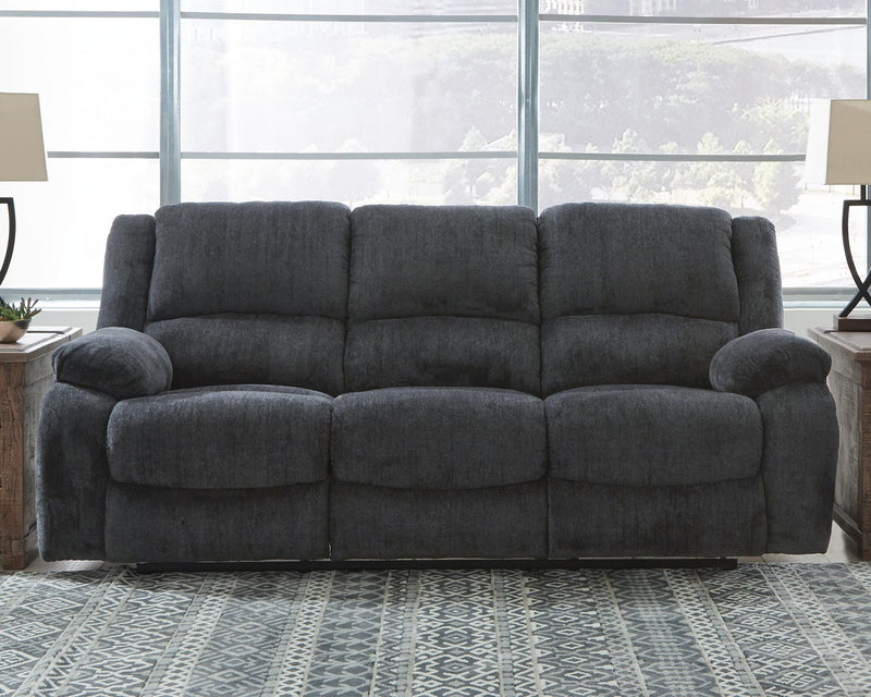 Ashley Furniture Draycoll reclining sofa shown in open position with plush cushions and dark upholstery in a modern living room setting.