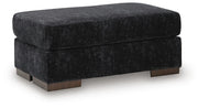 Ashley Furniture Whitmore Manor Ottoman with dark wood legs and upholstered fabric, shown from an angled side view.