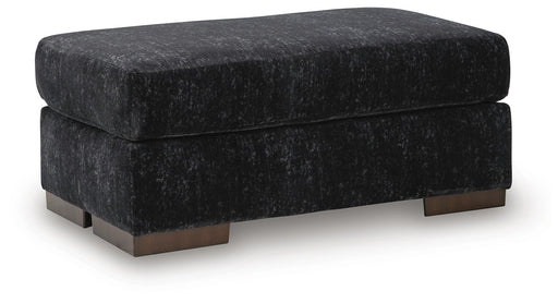 Ashley Furniture Whitmore Manor Ottoman with dark wood legs and upholstered fabric, shown from an angled side view.