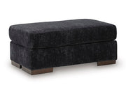 Ashley Furniture Whitmore Manor Ottoman in beige fabric with wooden block legs, shown from an angled perspective.