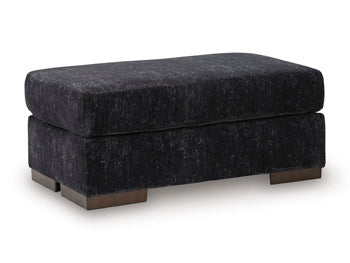 Ashley Furniture Whitmore Manor Ottoman in beige fabric with wooden block legs, shown from an angled perspective.