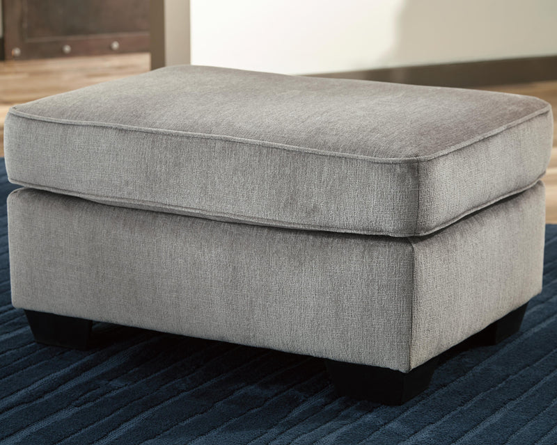 Ashley Furniture Altari Ottoman with padded fabric top and wooden legs, showing a close-up of the stylish living room accent piece.