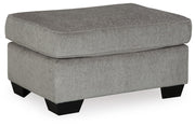 Ashley Furniture Altari Ottoman with a soft fabric cushion and wooden legs, shown from an angled side view.