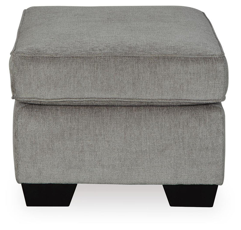 Ashley Furniture Altari Ottoman showing a plush, beige fabric upholstered ottoman with wooden legs in a living room setting.