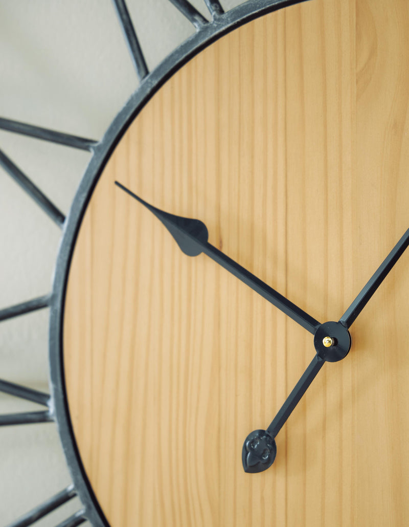 Ashley Furniture Brockett wall clock with a round wooden frame and vintage-style clock face, hanging on a white wall.