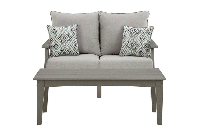 Ashley Furniture Visola outdoor loveseat and coffee table set with cushioned seating and wooden table in a backyard setting.