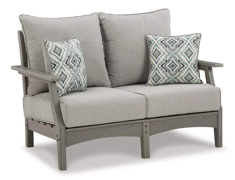 Outdoor Ashley Furniture Visola loveseat conversation set with cushioned seats and matching coffee table in a backyard patio setting.