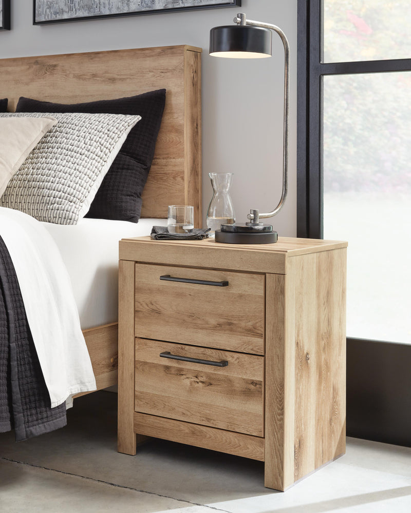 Ashley Furniture Hyanna Nightstand with wood finish, featuring two drawers and modern design, placed beside a bed.