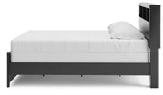 Ashley Furniture Broachmyn Bed with a wooden frame and upholstered headboard, shown from a side angle in a bedroom setting.