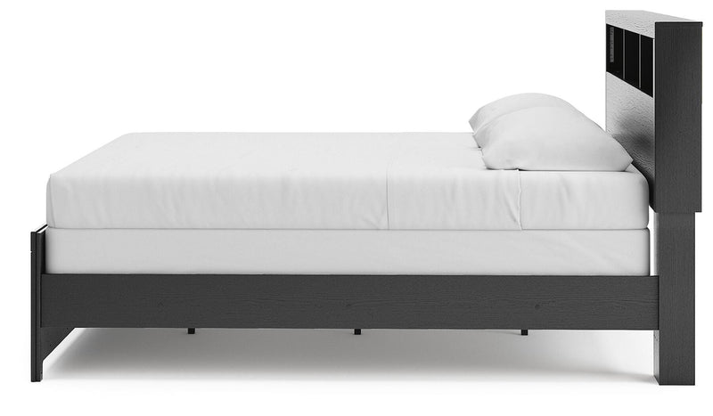 Ashley Furniture Broachmyn Bed with a wooden frame and upholstered headboard, shown from a side angle in a bedroom setting.