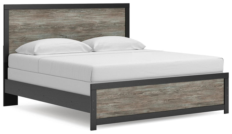 Ashley Furniture Broachmyn Bed with a wooden headboard and frame, shown from a side angle in a bedroom setting.