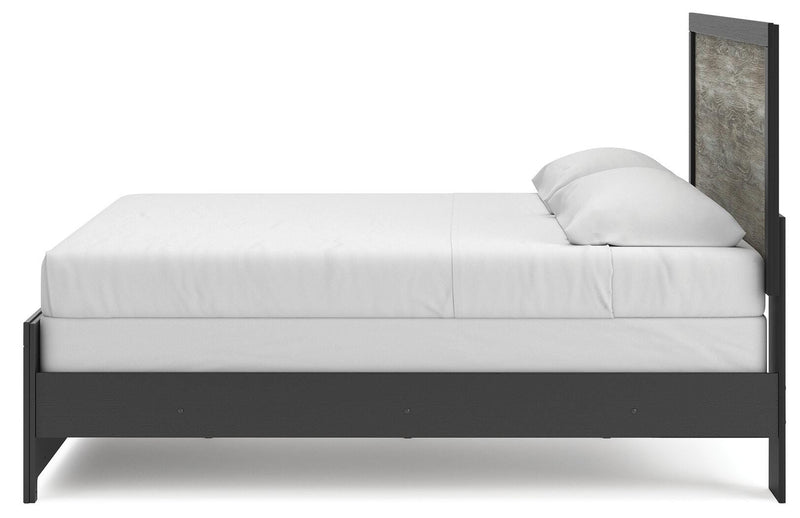 Ashley Furniture Broachmyn Bed with a wooden frame and headboard, shown from a side angle in a modern bedroom setting.