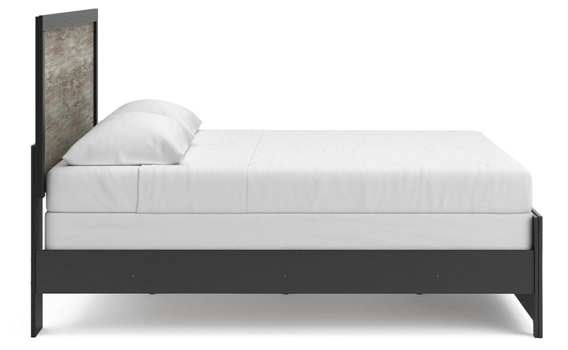 Ashley Furniture Broachmyn Bed with a wooden frame and headboard, shown from a side angle in a bedroom setting.