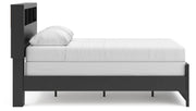 Ashley Furniture Broachmyn Bed with a wooden frame and headboard, shown from the side in a cozy bedroom setting.