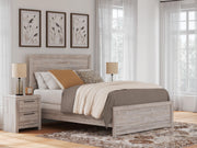 Ashley Furniture Broachmyn Bed with tufted headboard and wooden frame, shown in a cozy bedroom setting.