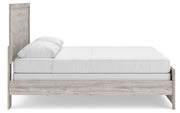 Ashley Furniture Broachmyn Bed with beige upholstered headboard and wooden frame, shown from a side angle in a bedroom setting.