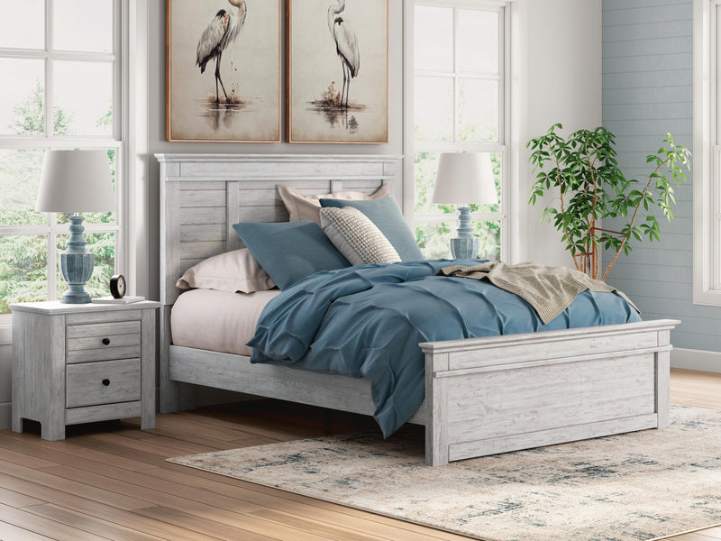 Ashley Furniture Makidern bed with a wooden frame and upholstered headboard, shown in a modern bedroom setting.