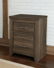 Ashley Furniture Juararo nightstand with dark wood finish and sleek drawer handles, shown in a modern bedroom setting.