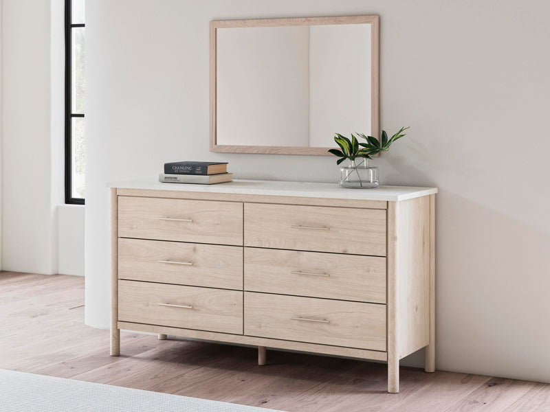 Ashley Furniture Cadmori bedroom mirror, rectangular with beveled glass and wood frame, hangs on a wall in a modern bedroom setting.