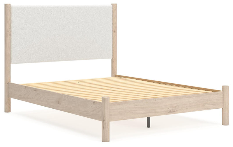 Ashley Furniture Cadmori upholstered bed with a padded headboard, shown from a side angle in a modern bedroom setting.