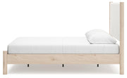 Ashley Furniture Cadmori upholstered bed with beige fabric, tufted headboard, and wooden legs, shown from a side angle.