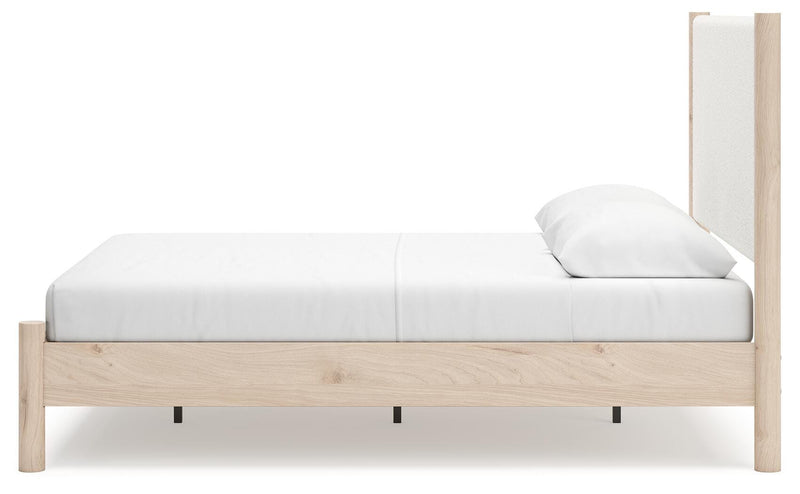Ashley Furniture Cadmori upholstered bed with beige fabric, tufted headboard, and wooden legs, shown from a side angle.