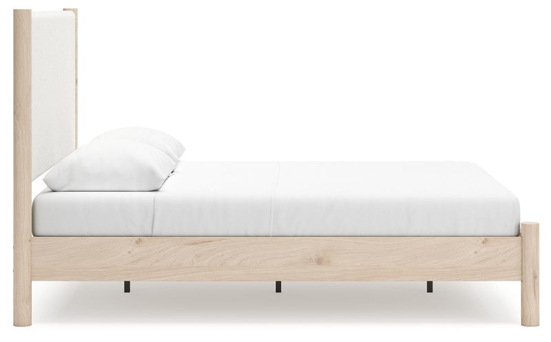 Ashley Furniture Cadmori upholstered bed with plush fabric and padded headboard, shown from a side angle in a modern bedroom setting.