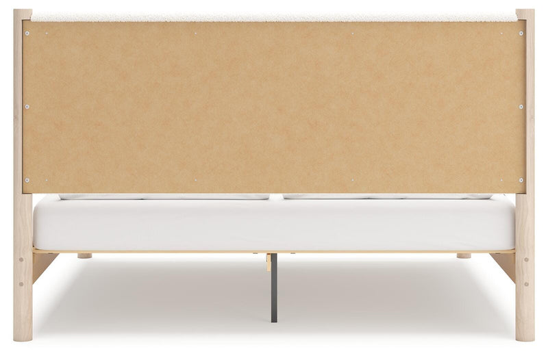 Ashley Furniture Cadmori upholstered bed with a tall, padded headboard and elegant fabric upholstery, shown from the back.