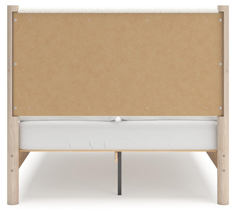Ashley Furniture Cadmori upholstered bed with a padded headboard and neutral fabric, shown from the back in a modern bedroom setting.